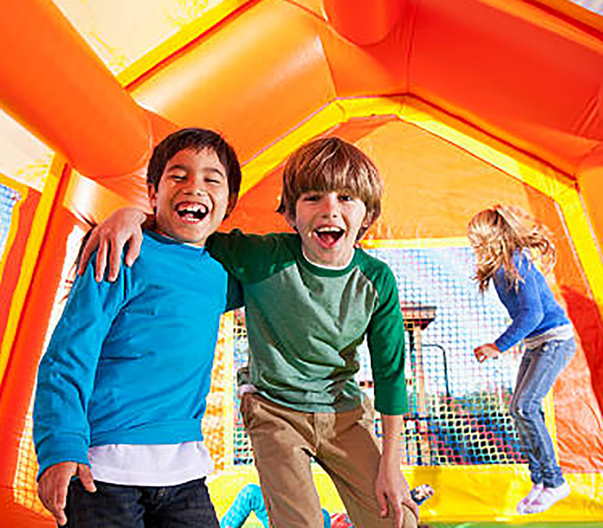 Multi-ethnic boys laughing in bouncy castle, girls jumping in background.